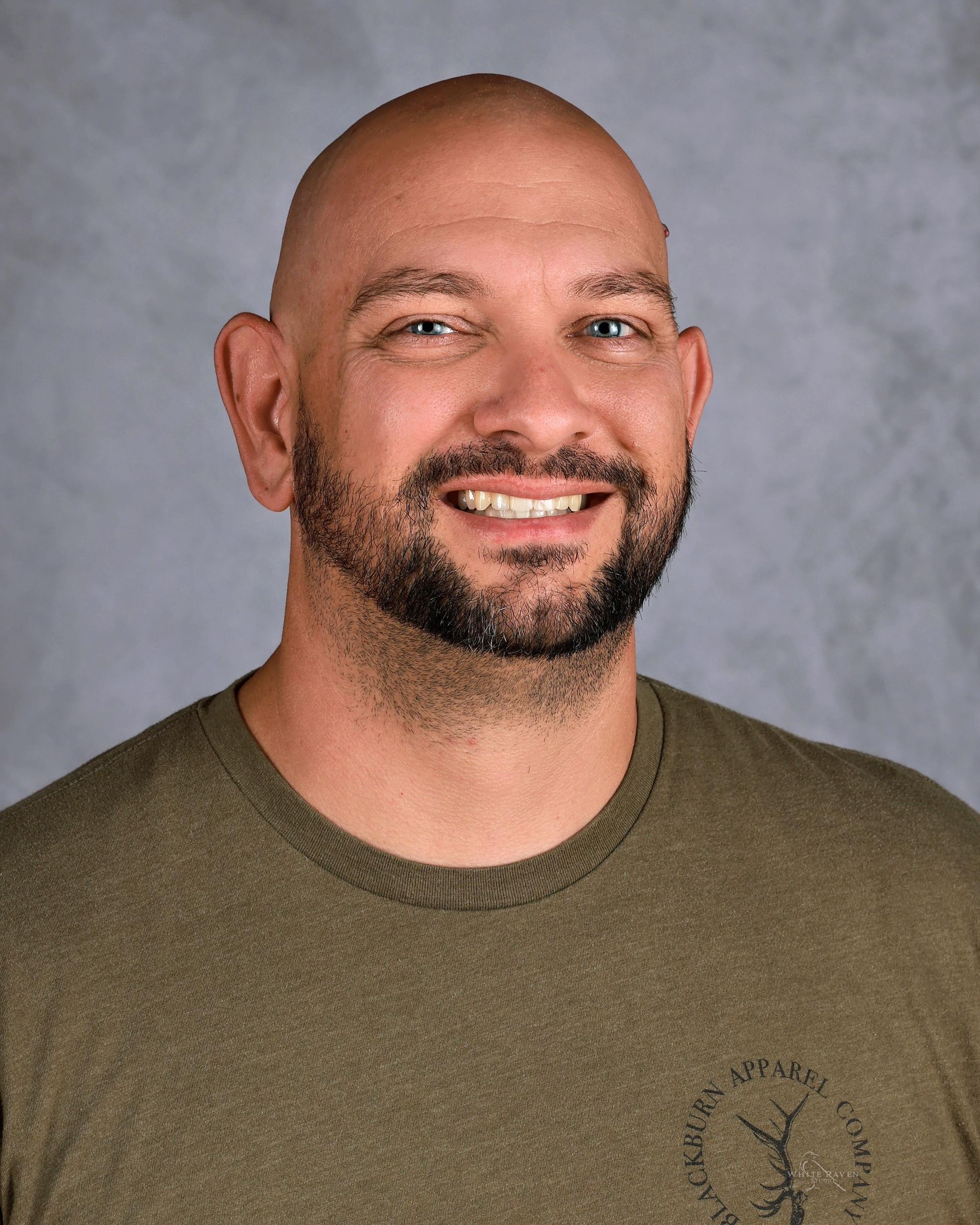 Smiling bald man with a beard, wearing a green shirt against a gray background.