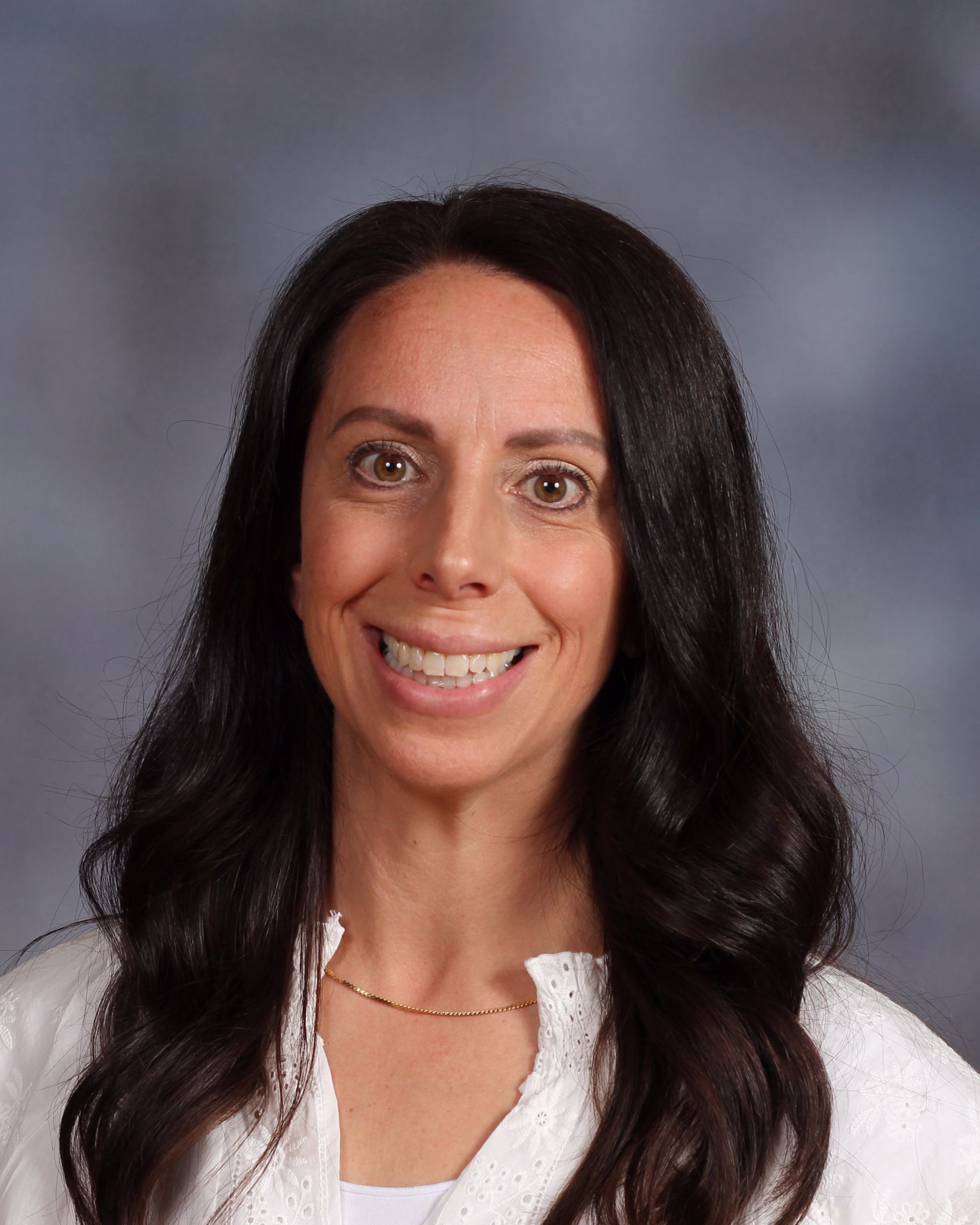 A woman with long dark hair is smiling and wearing a white shirt.