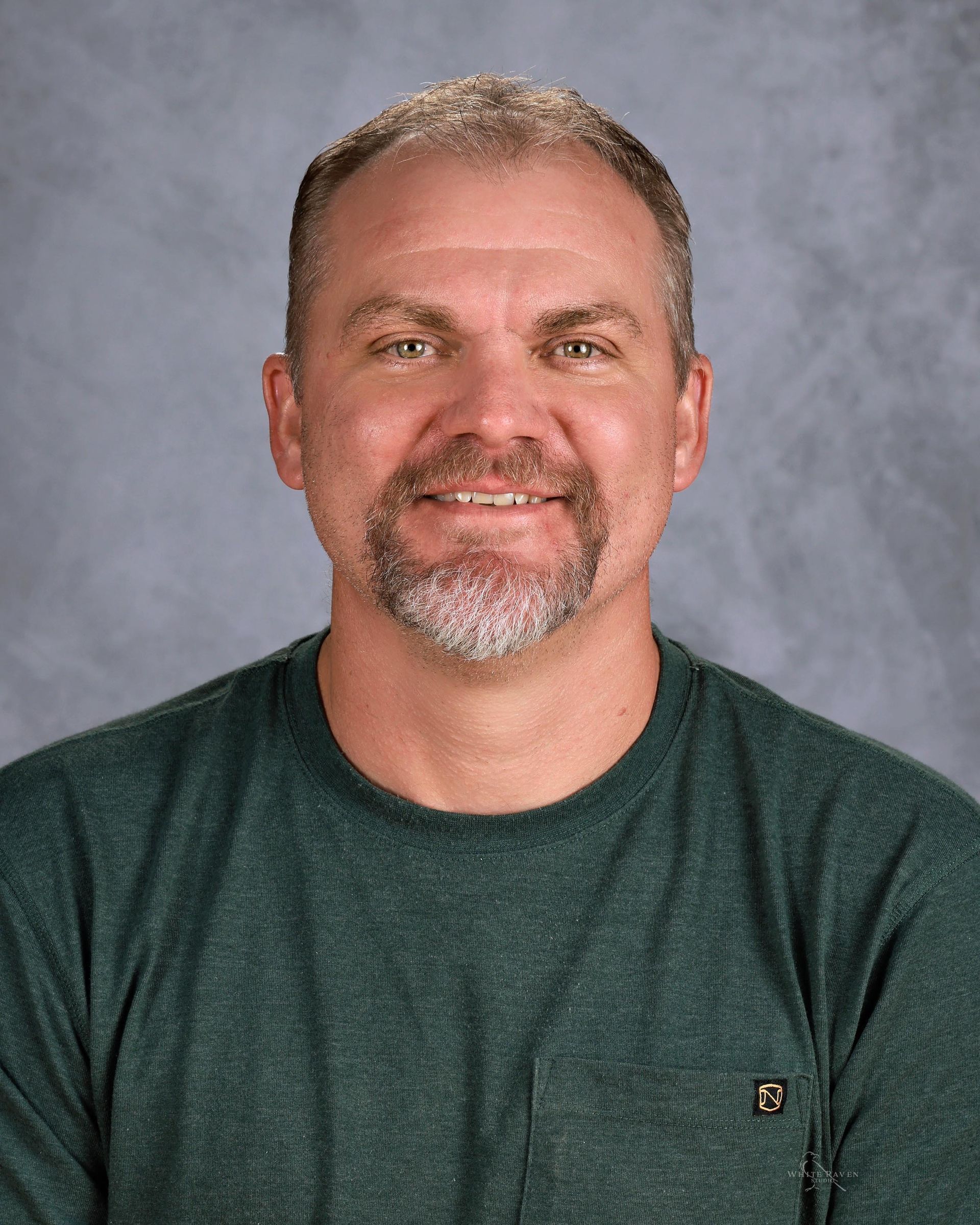 Man with graying hair and goatee smiles, wearing a green shirt.