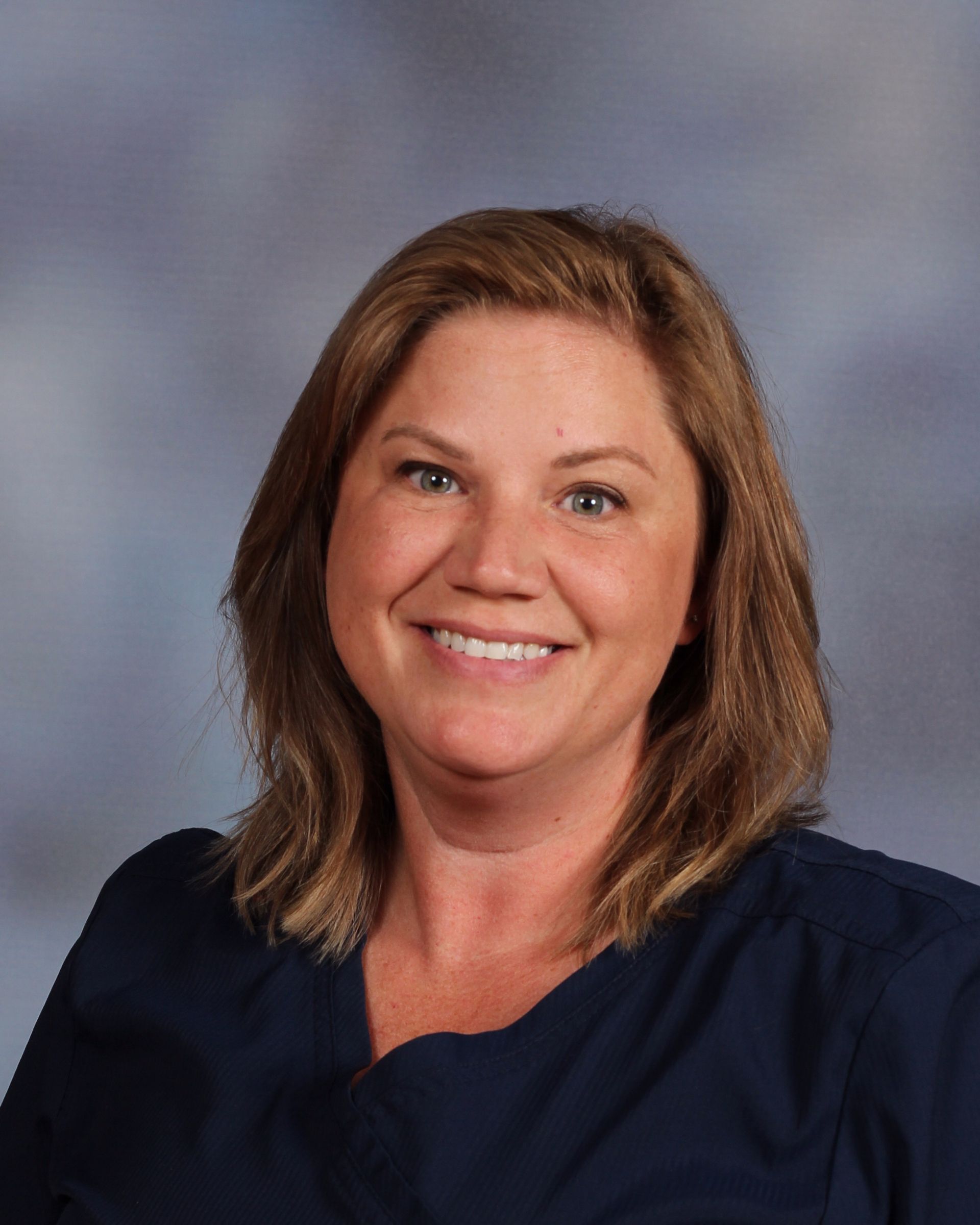 A woman in a blue shirt is smiling for the camera.