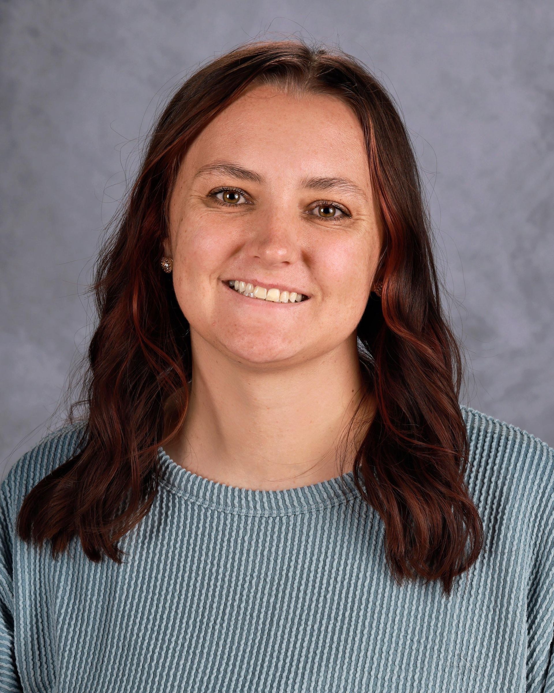 Woman with brown hair smiling, wearing a blue sweater, against a gray background.