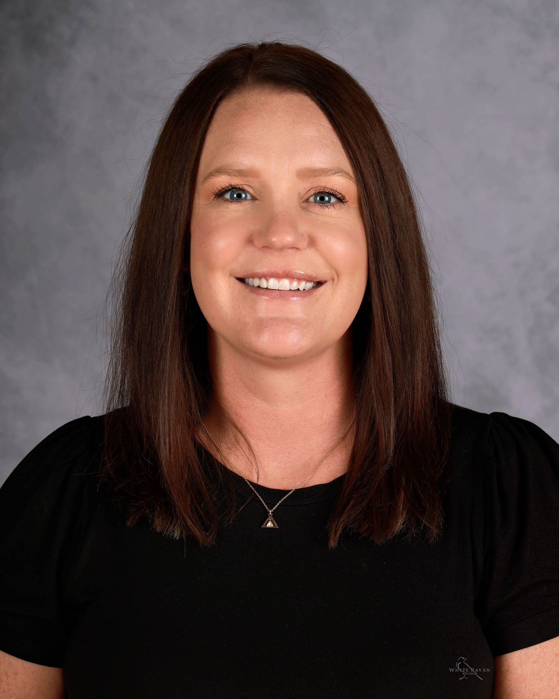 Woman with brown hair, smiling, wearing a black top against a gray background.