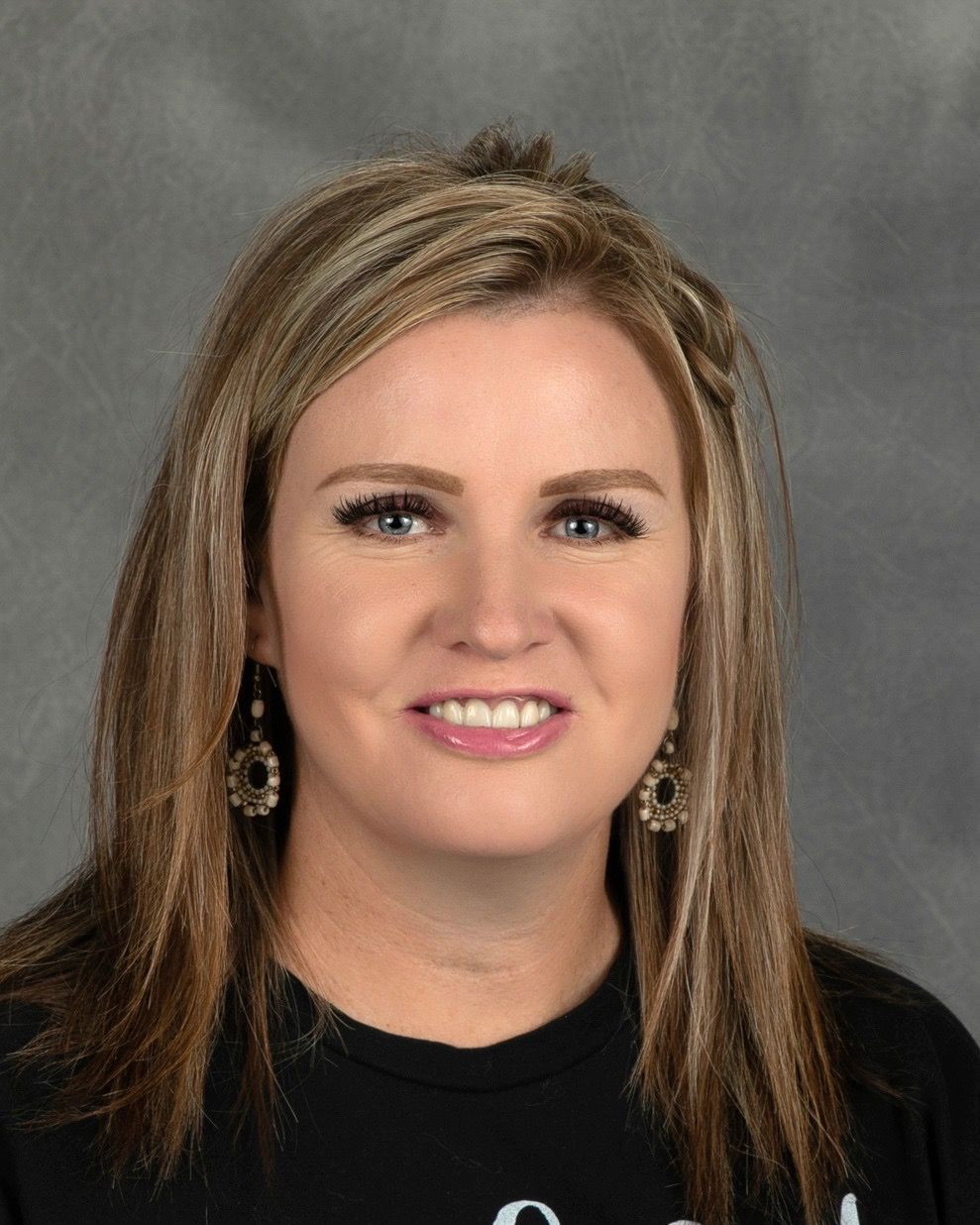 A woman wearing a black shirt and earrings is smiling for the camera.