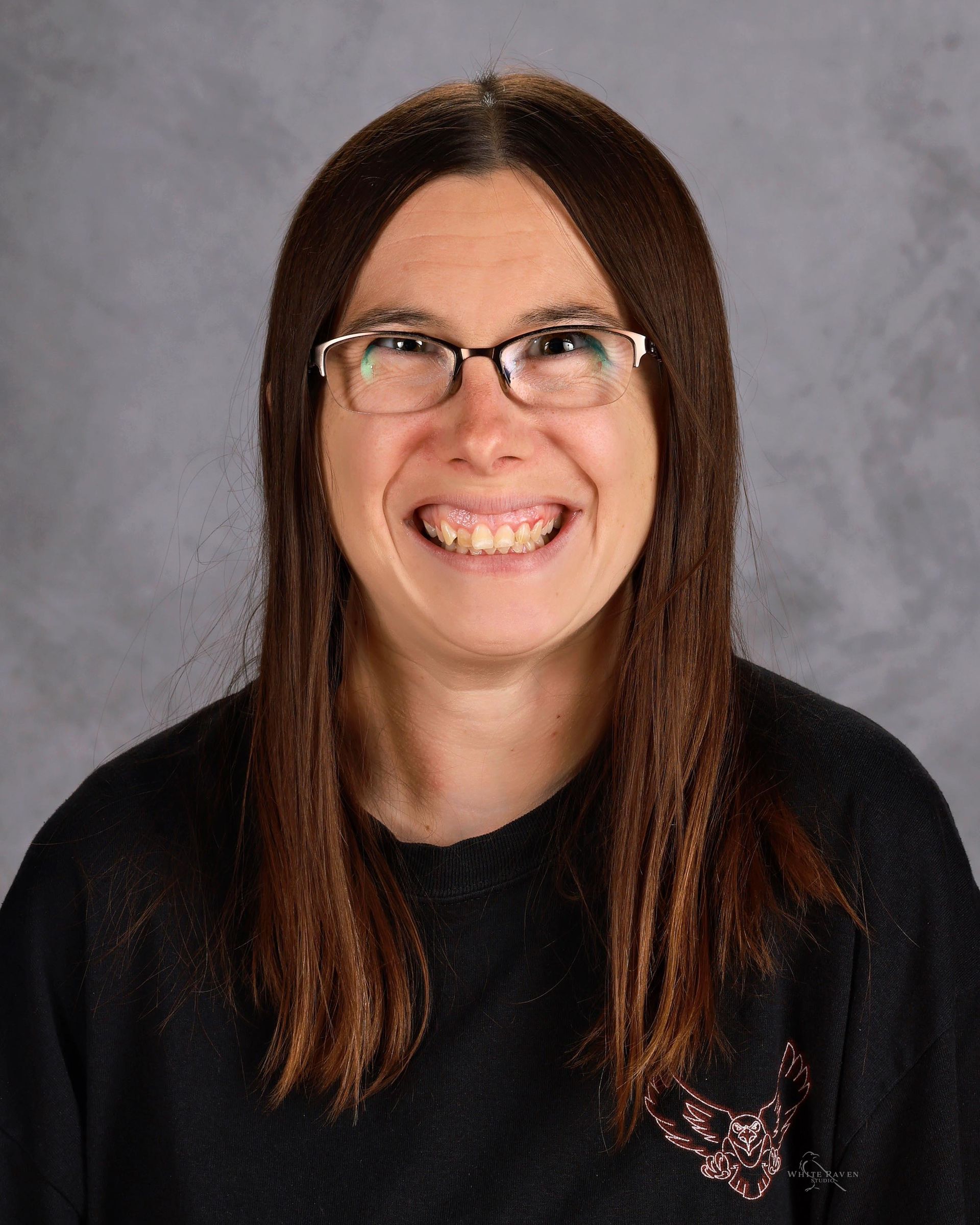 Woman with glasses, long brown hair, smiling, wearing a black sweatshirt, against a gray background.