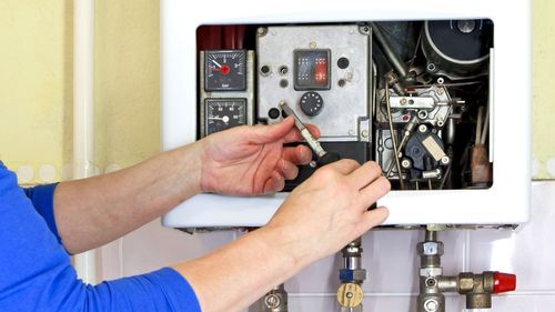 A person is fixing a water heater with a screwdriver.
