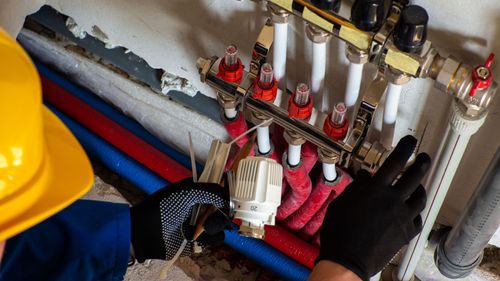 A man wearing a hard hat and gloves is working on a heating system.