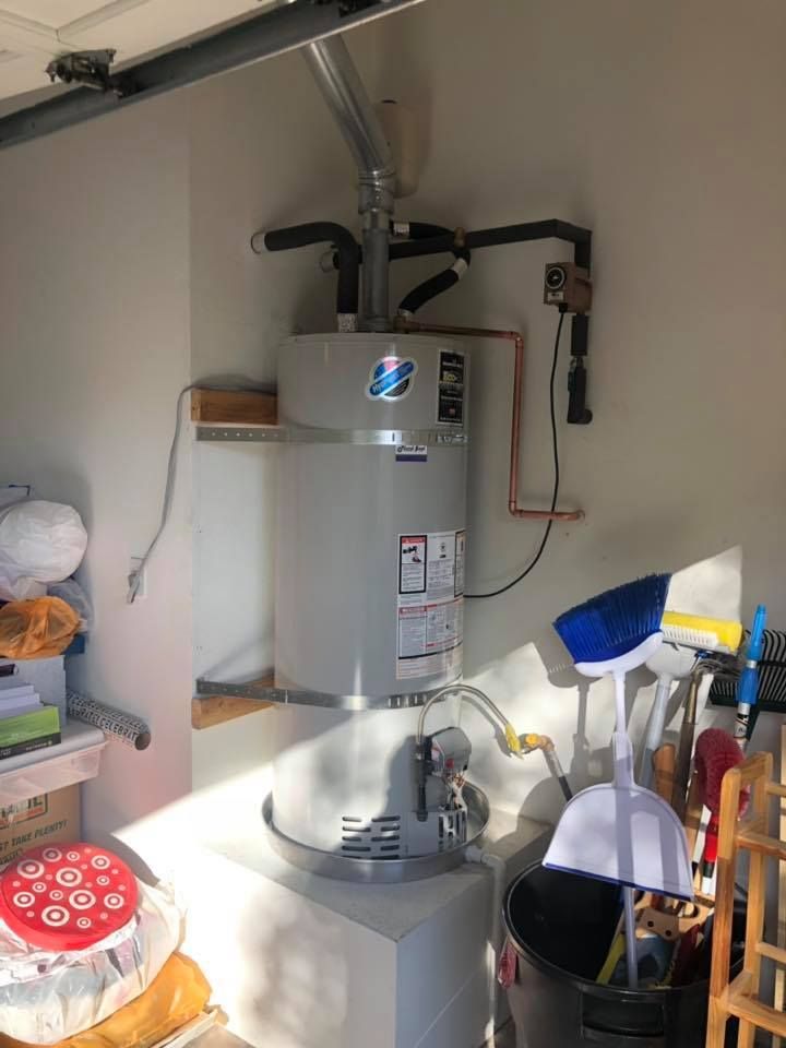 A water heater is sitting in a garage next to a washer and dryer.