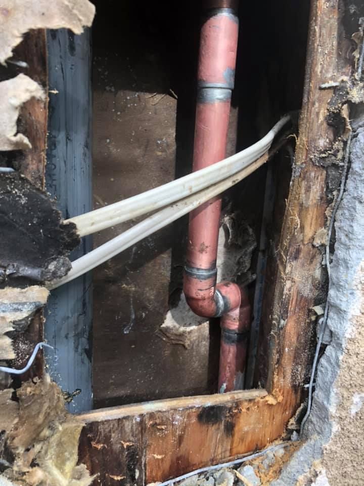 A red pipe is coming out of a hole in a wall.
