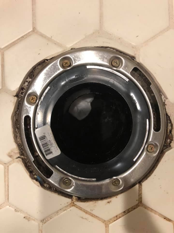 A close up of a toilet flange on a tiled floor.