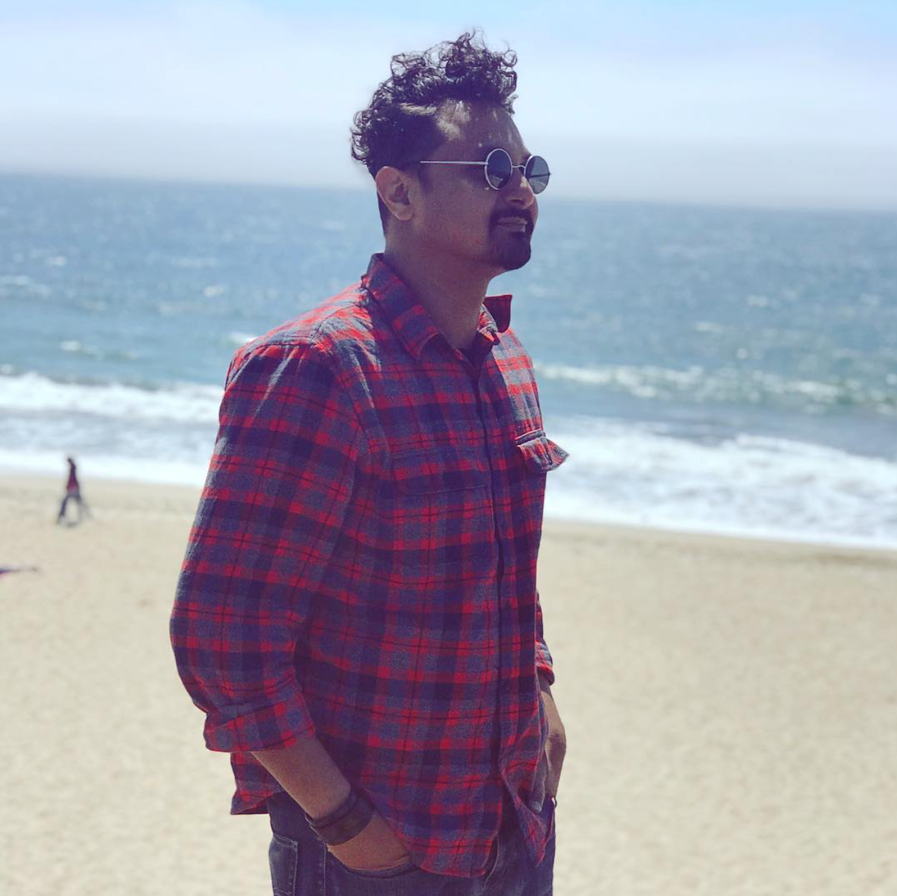 A man wearing sunglasses and a plaid shirt is standing on a beach