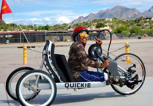 Person in a red helmet driving a white tricycle on a road with mountains in the background