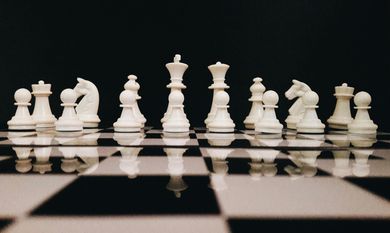 Chess pieces set up on a chessboard, white pieces against a dark background.