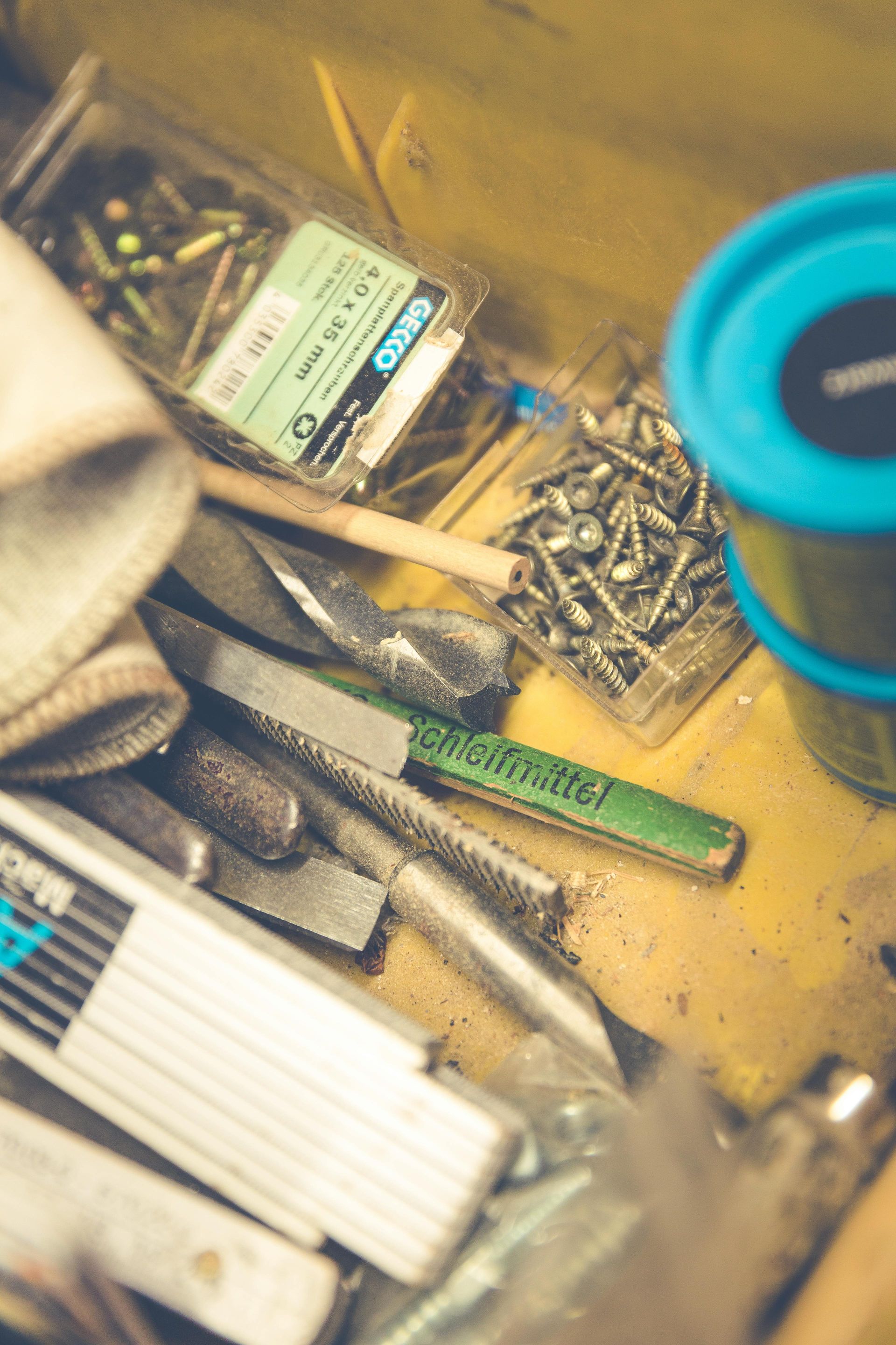 Tools and hardware in a yellow toolbox, including screws, drill bits, and a green handled file.
