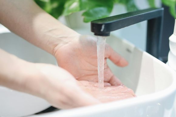 Person washing hands under a black faucet in a white sink.