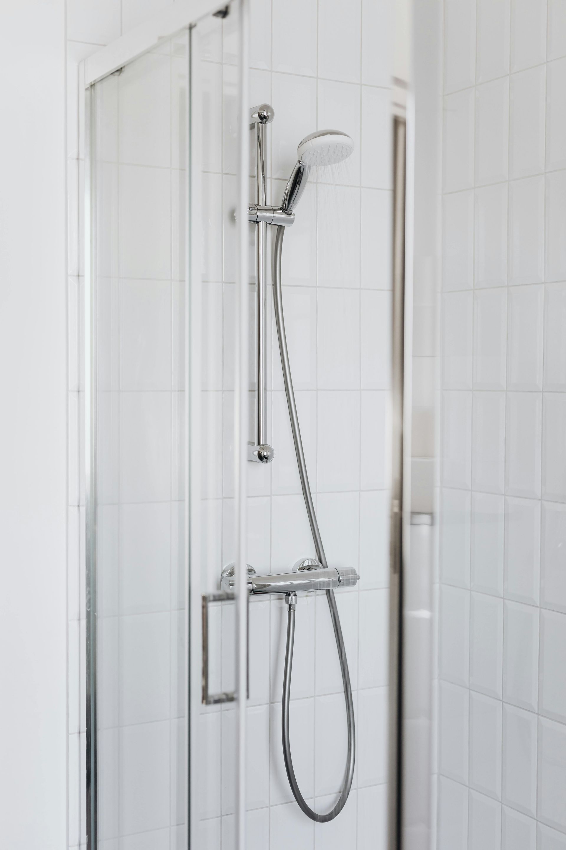 Shower stall with white tile, chrome fixtures, and a glass door.