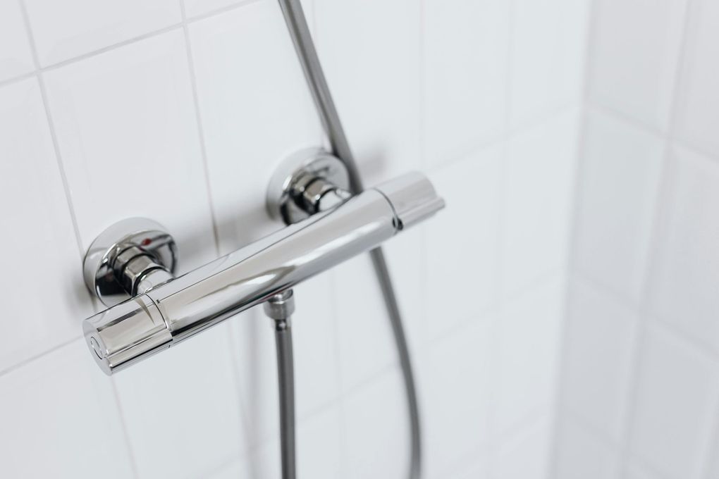 Chrome shower fixture on white tiled wall, with a hand-held shower.