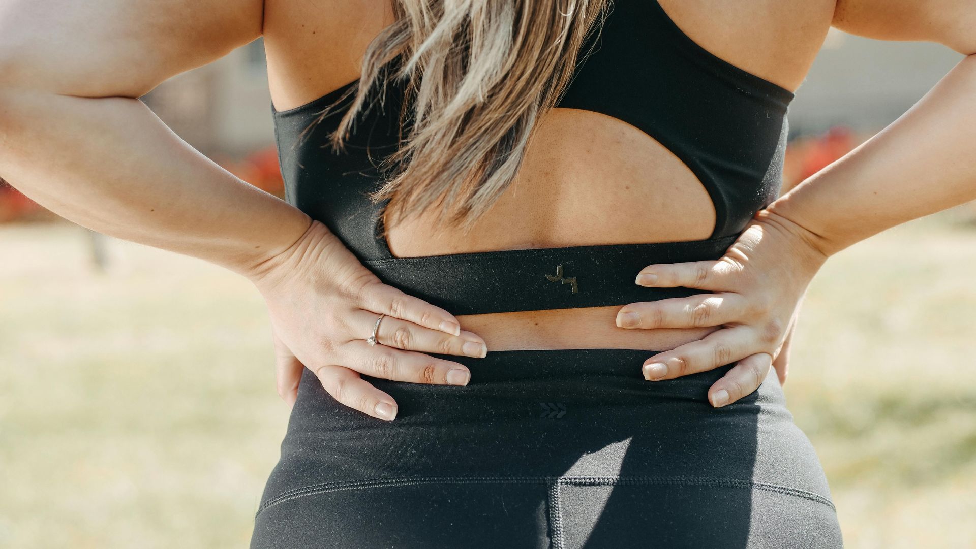Woman in black workout clothes holds her back, outdoors.