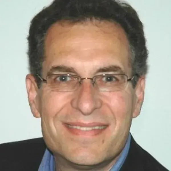 Man with glasses smiling, wearing a blue shirt and black blazer.