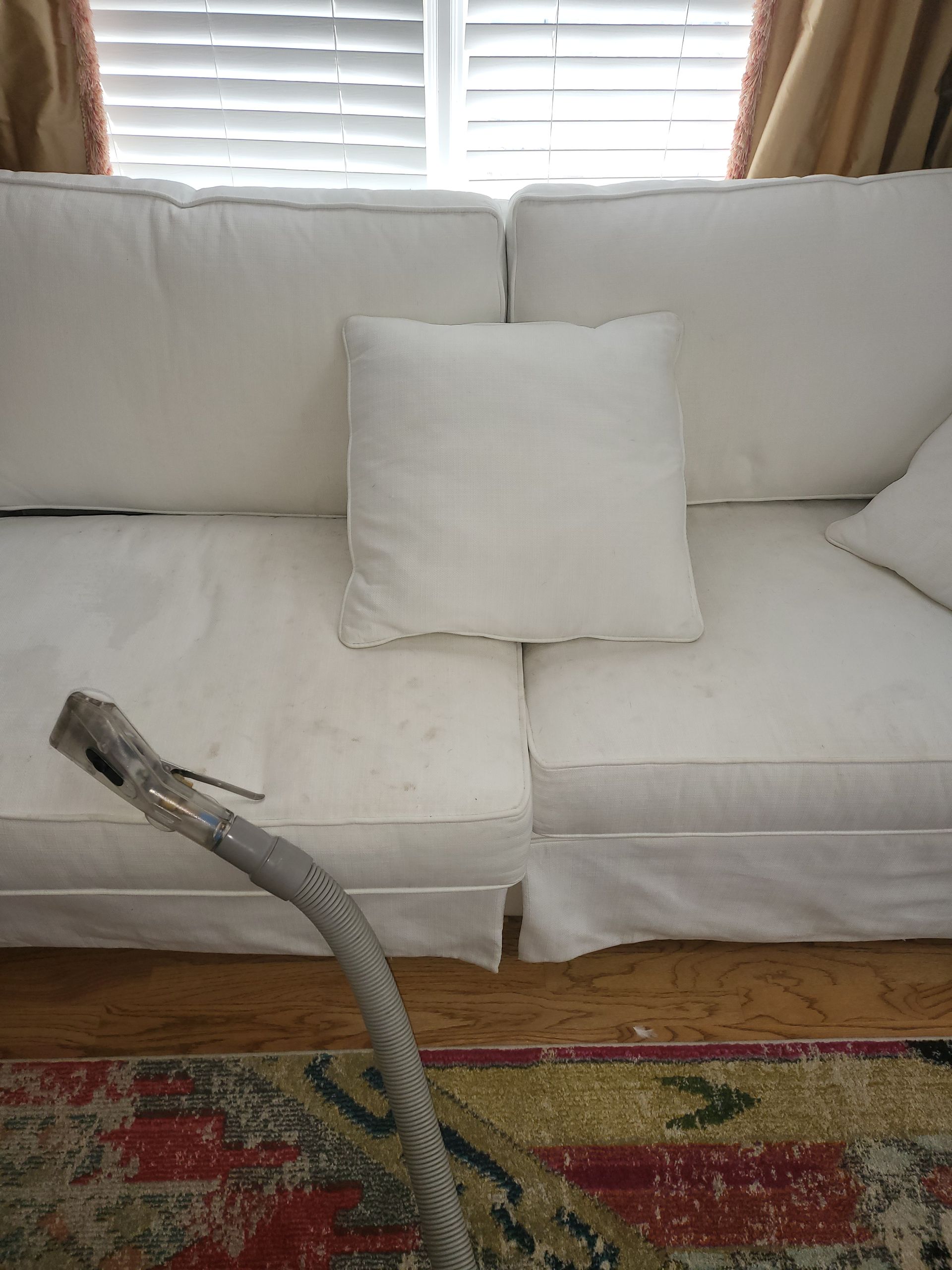 A white couch with a vacuum cleaner attached to it in a living room.