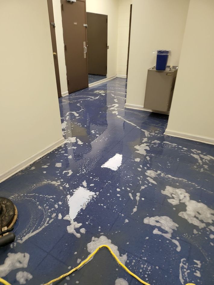 Blue tiled floor covered in cleaning solution in a hallway with closed brown doors and off-white walls.