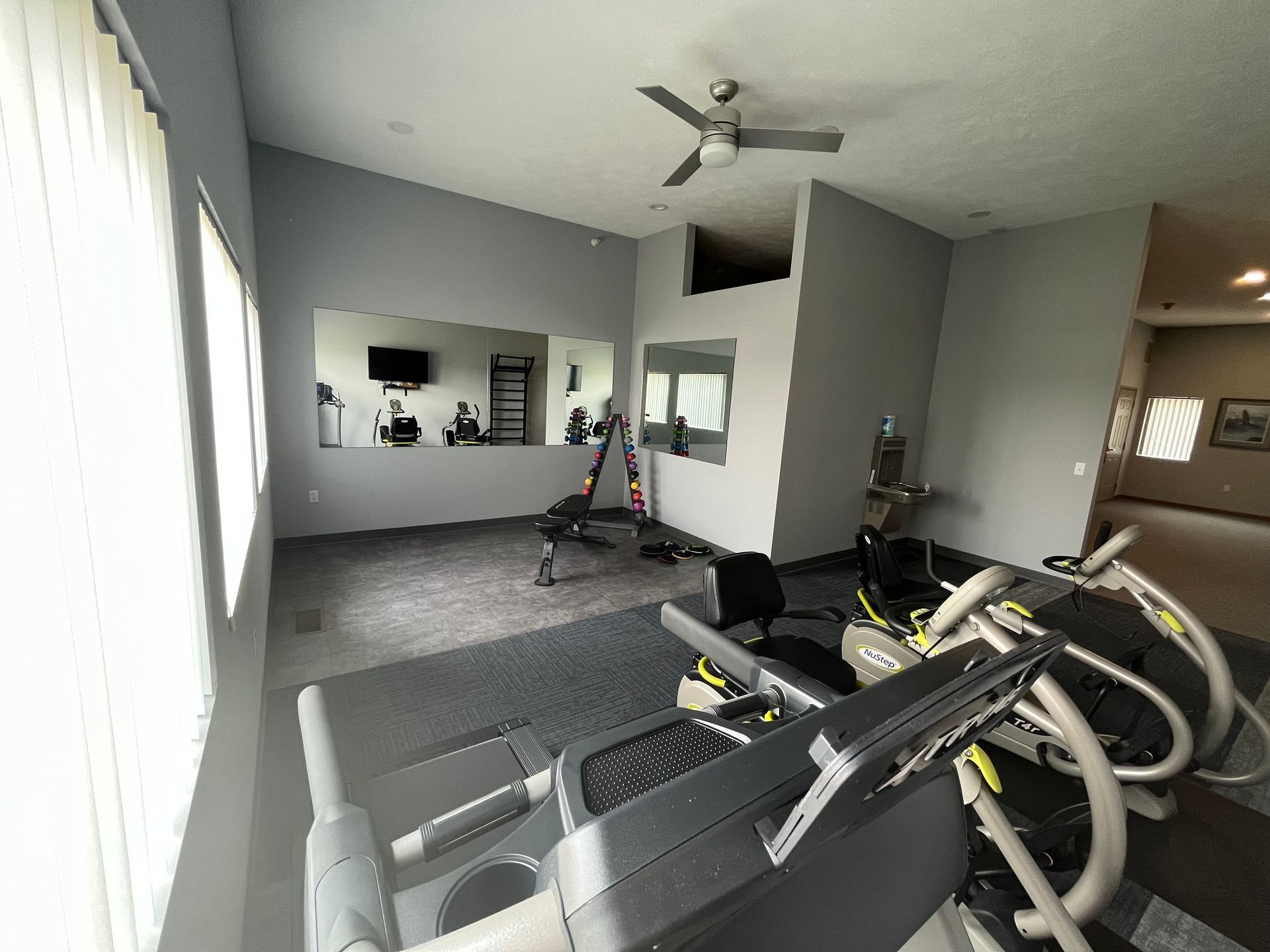 a gym with a treadmill , elliptical , and a ceiling fan .