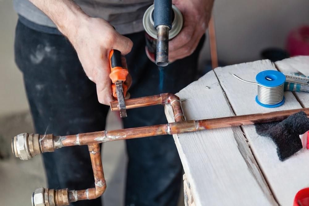 A man is cutting a copper pipe with a saw.