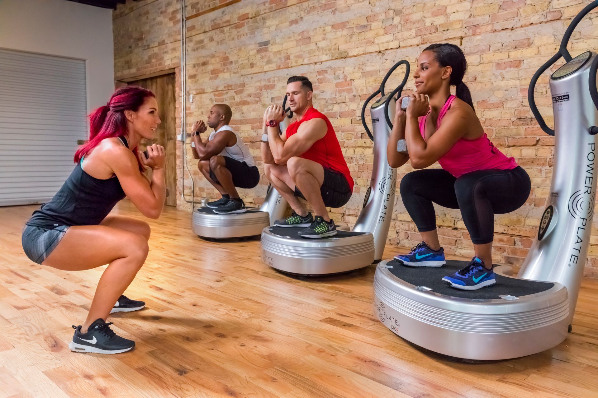 A group of people are squatting on power plate machines in a gym.