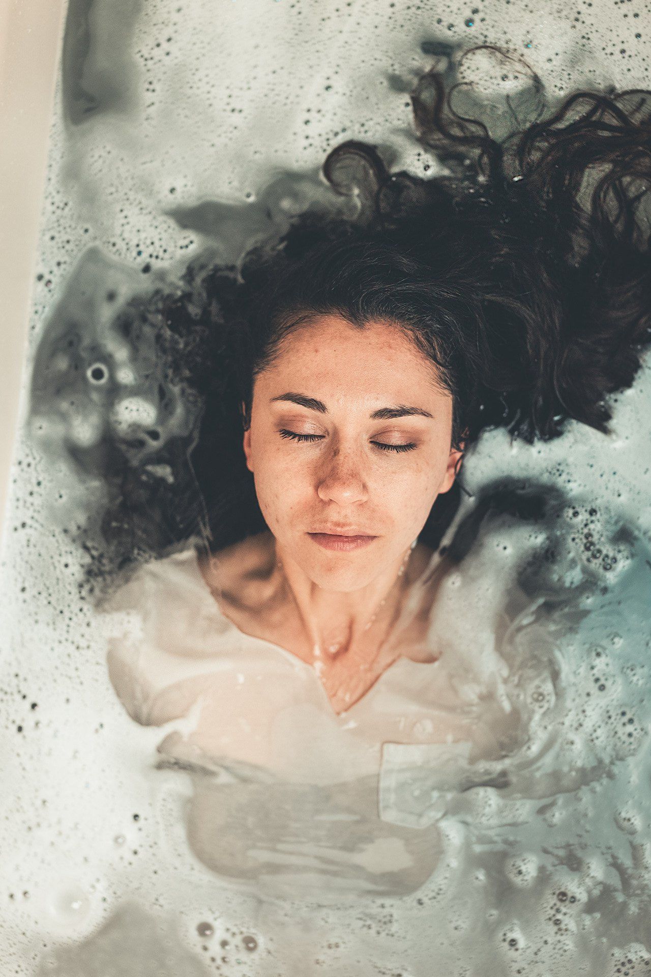 A woman is laying in a bathtub with her eyes closed.