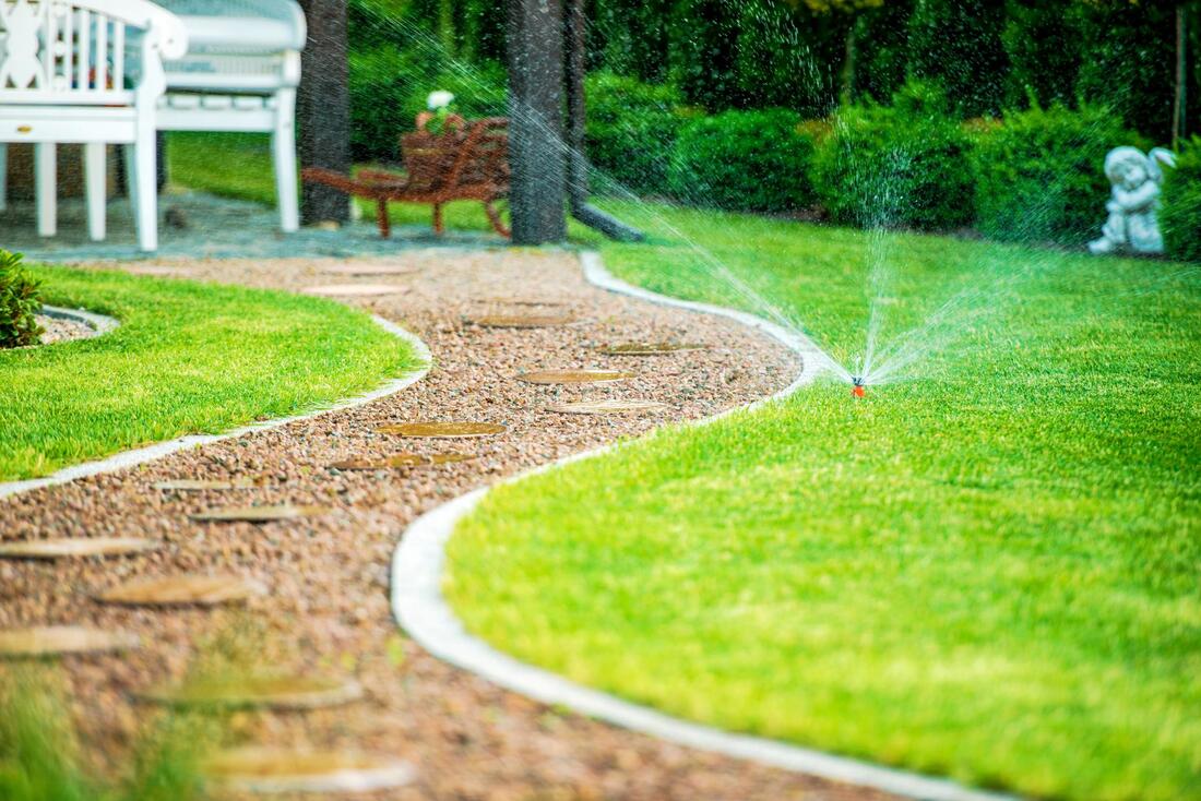 river rock pathway through a well landscaped yard with a sprinkler on