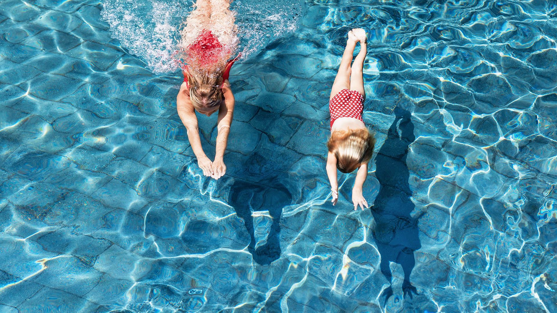 Two young girls are diving into a swimming pool.