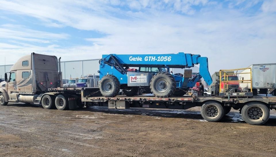 a semi truck is carrying a boom lift on a flat bed trailer for Mandel rentals