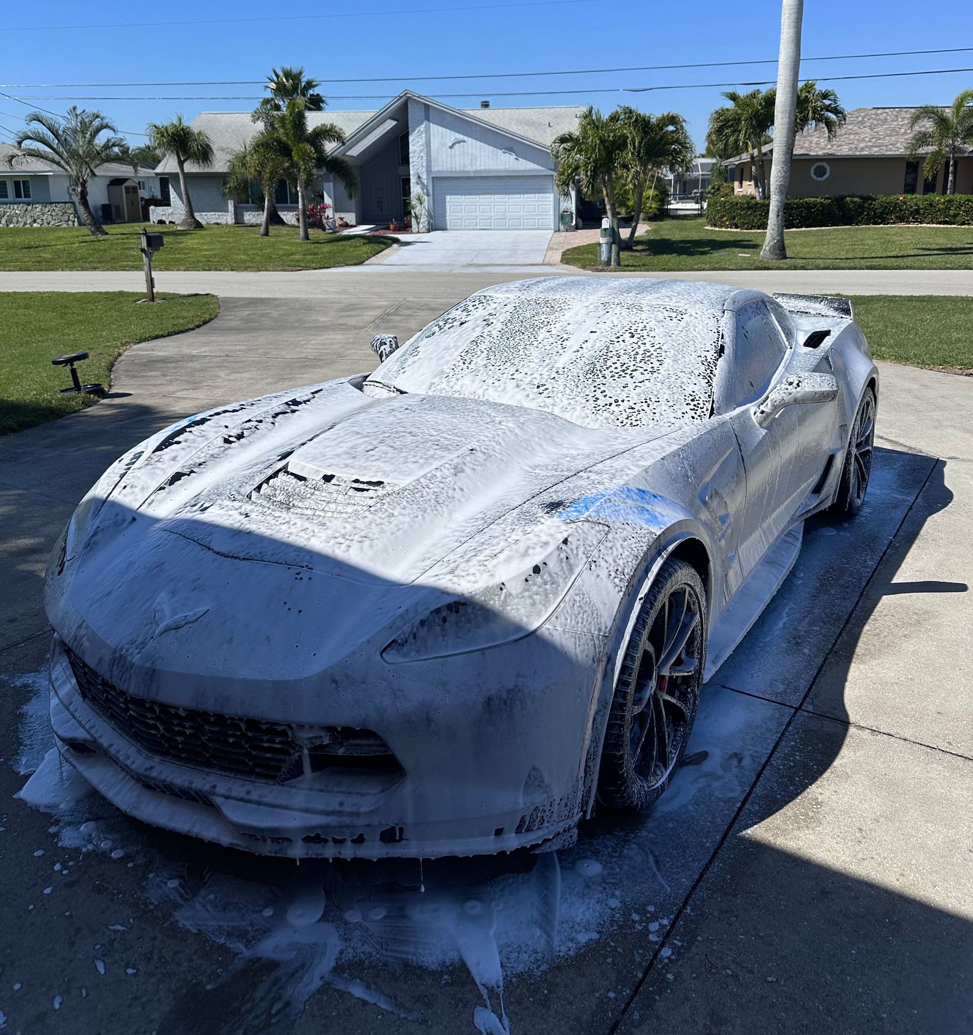 White sports car covered in soapy foam in a driveway.