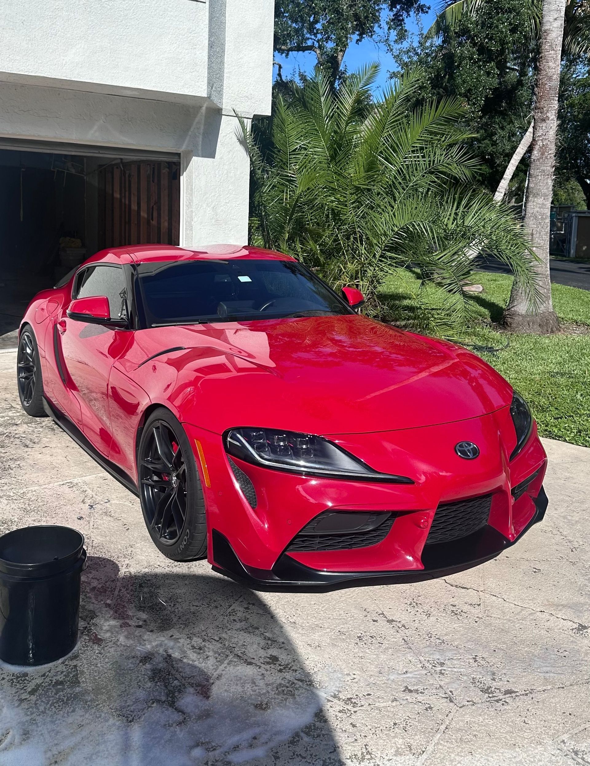 Red Toyota Supra sports car parked outside a garage; a bucket is visible.