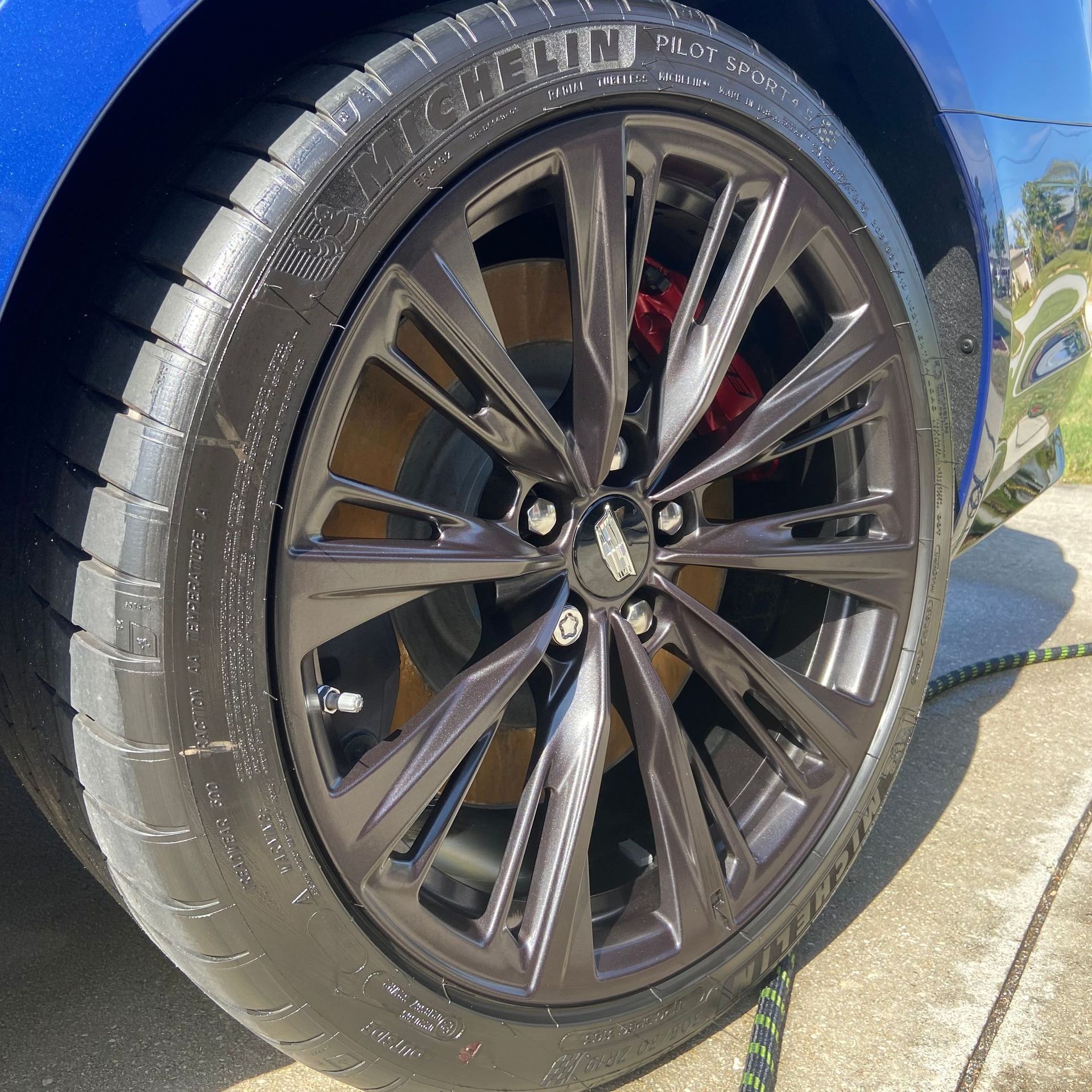 Blue car's black wheel with red brake caliper; Michelin tire, shiny rim, outdoors.