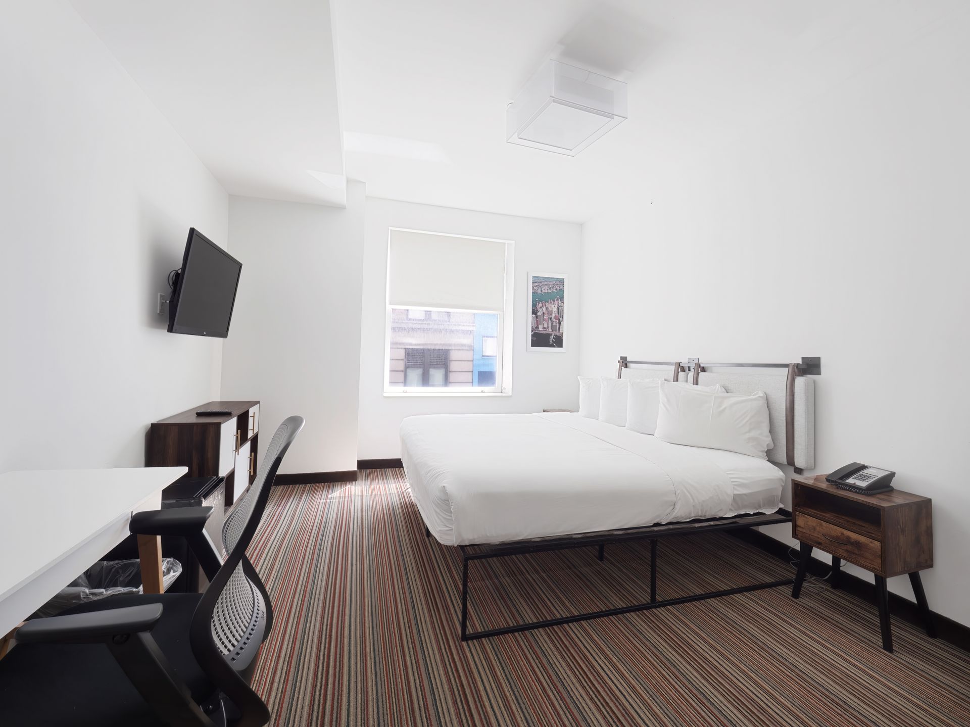 A hotel room with a king size bed , desk , chair and television.