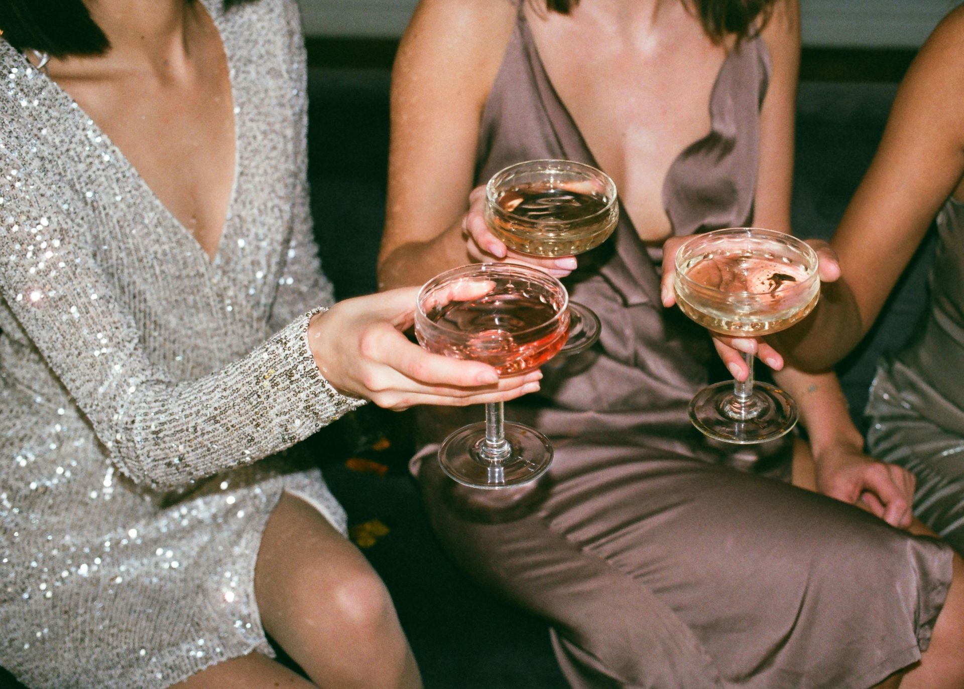 Three women are sitting on a couch holding champagne glasses.
