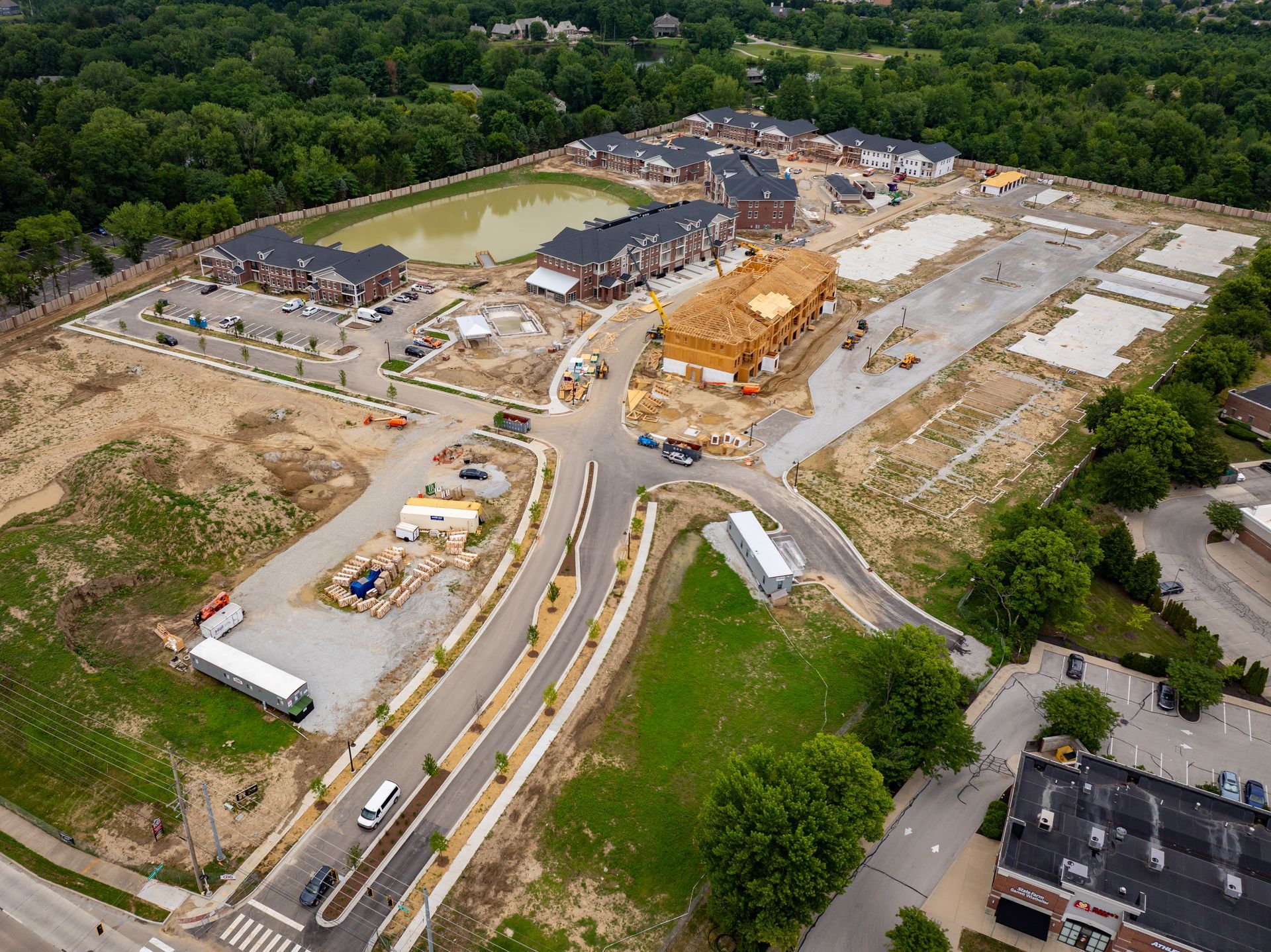 Aerial view of a construction site with partially built apartment buildings, a pond, and a road.