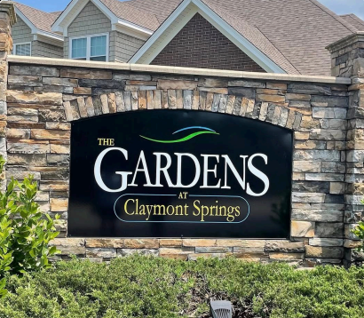 Stone entrance sign reading “The Gardens at Claymont Springs” in front of homes