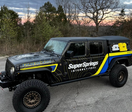 Black off-road truck with Super Springs branding and yellow-blue graphics parked outdoors at sunset