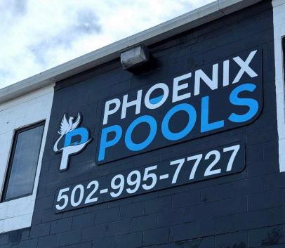 Phoenix Pools business sign on a dark building, with blue and white lettering and phone number 502-995-7727