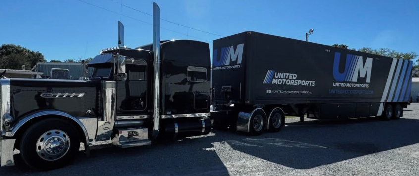 Black United Roadshow semi truck and trailer parked in a lot under a clear sky