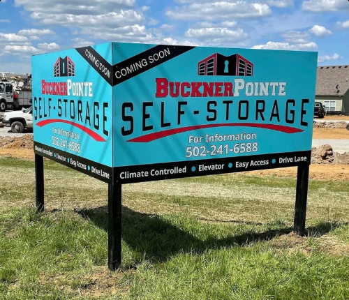 Buckner Pointe Self Storage roadside sign on a grassy lot, blue and black with “Coming Soon” text