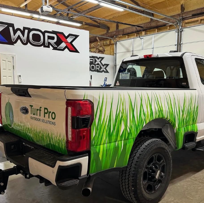 White pickup truck with green grass graphics parked indoors under WORX and Turf Pro signs