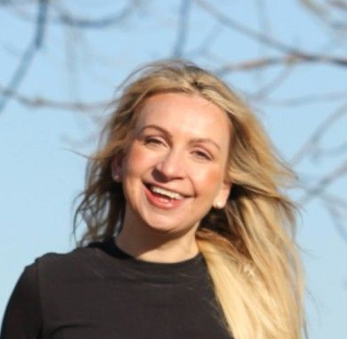 Lachende blonde vrouw in een zwarte top buiten tegen een blauwe lucht en elektriciteitskabels.