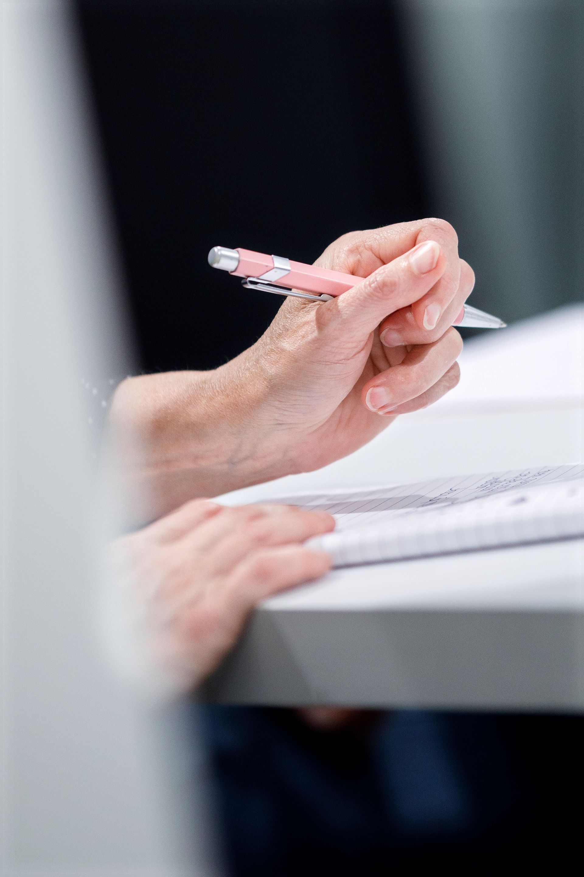 Hand die een roze pen boven papieren op een wit bureau houdt