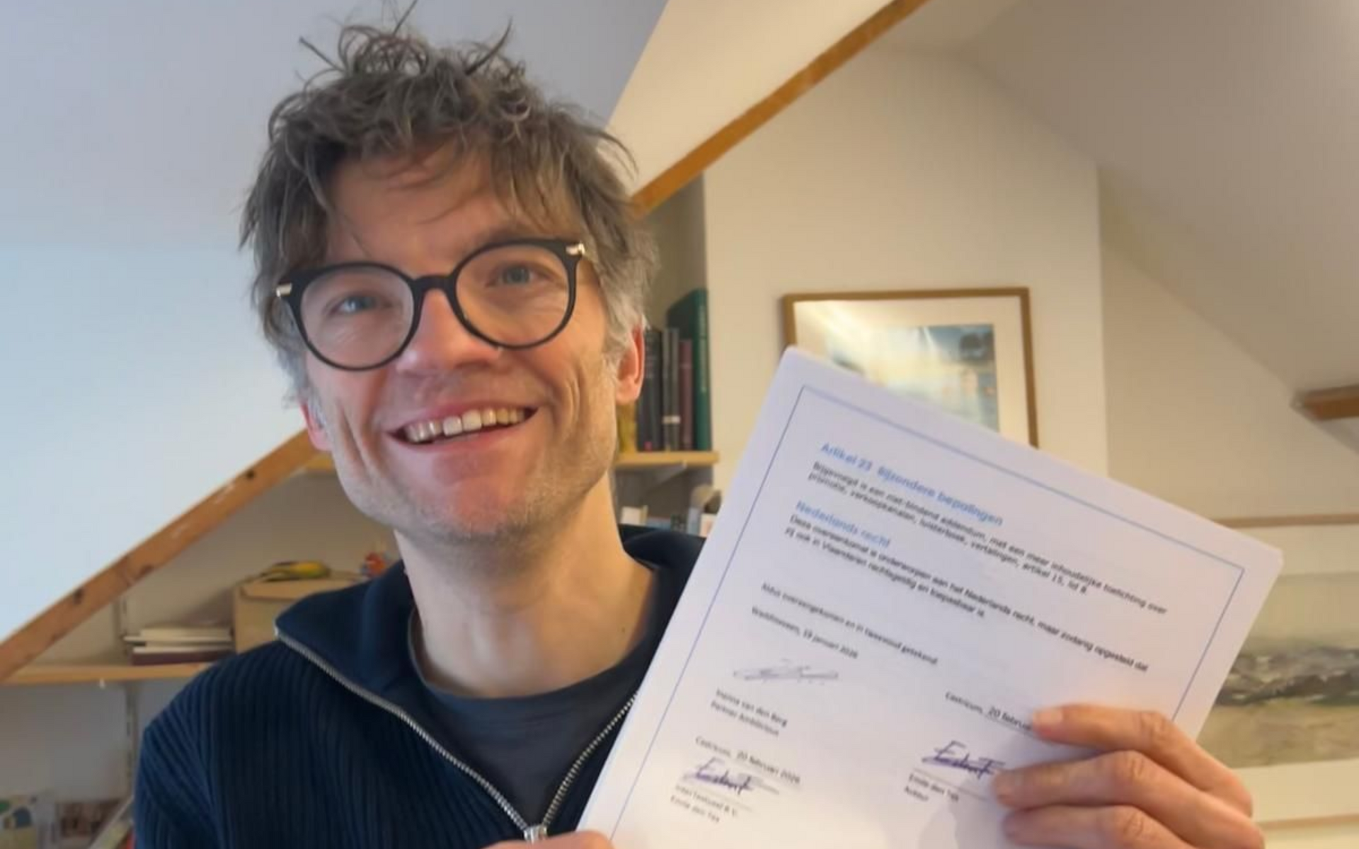 Een lachende persoon houdt een geprint document vast, binnen naast een trap.