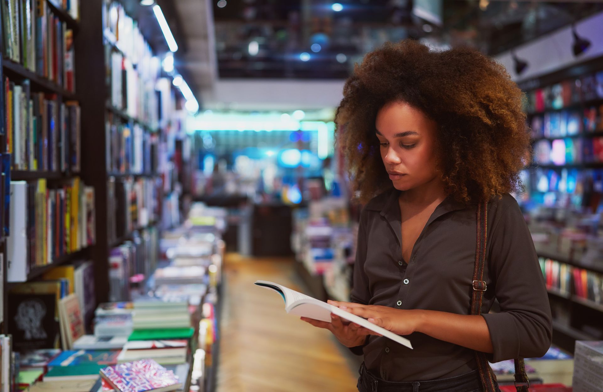Een vrouw leest een boek in een boekwinkel, terwijl ze door de schappen bladert in een helder verlichte winkel.