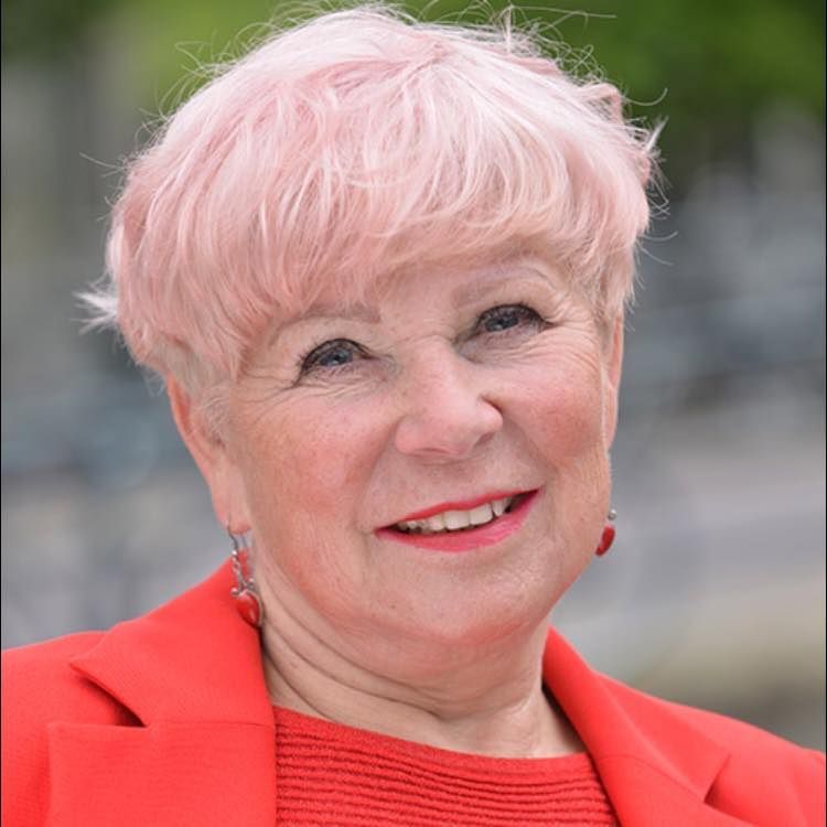 Lachende vrouw met kort roze haar en een rode blazer buiten.