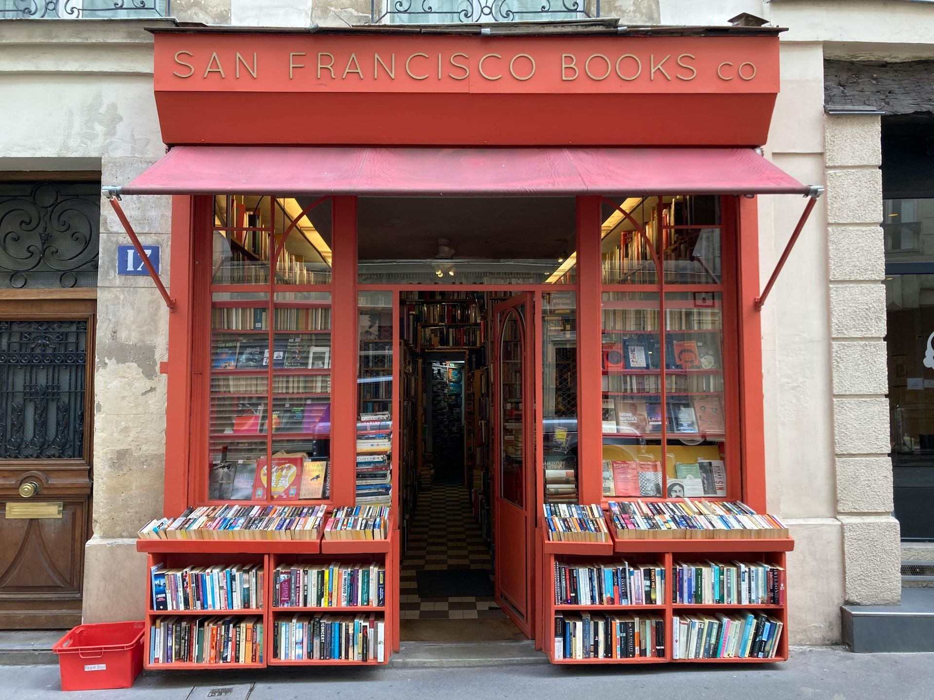Een boekhandel met een rode gevel, boeken die buiten uitgestald staan ​​en een bord met de tekst 