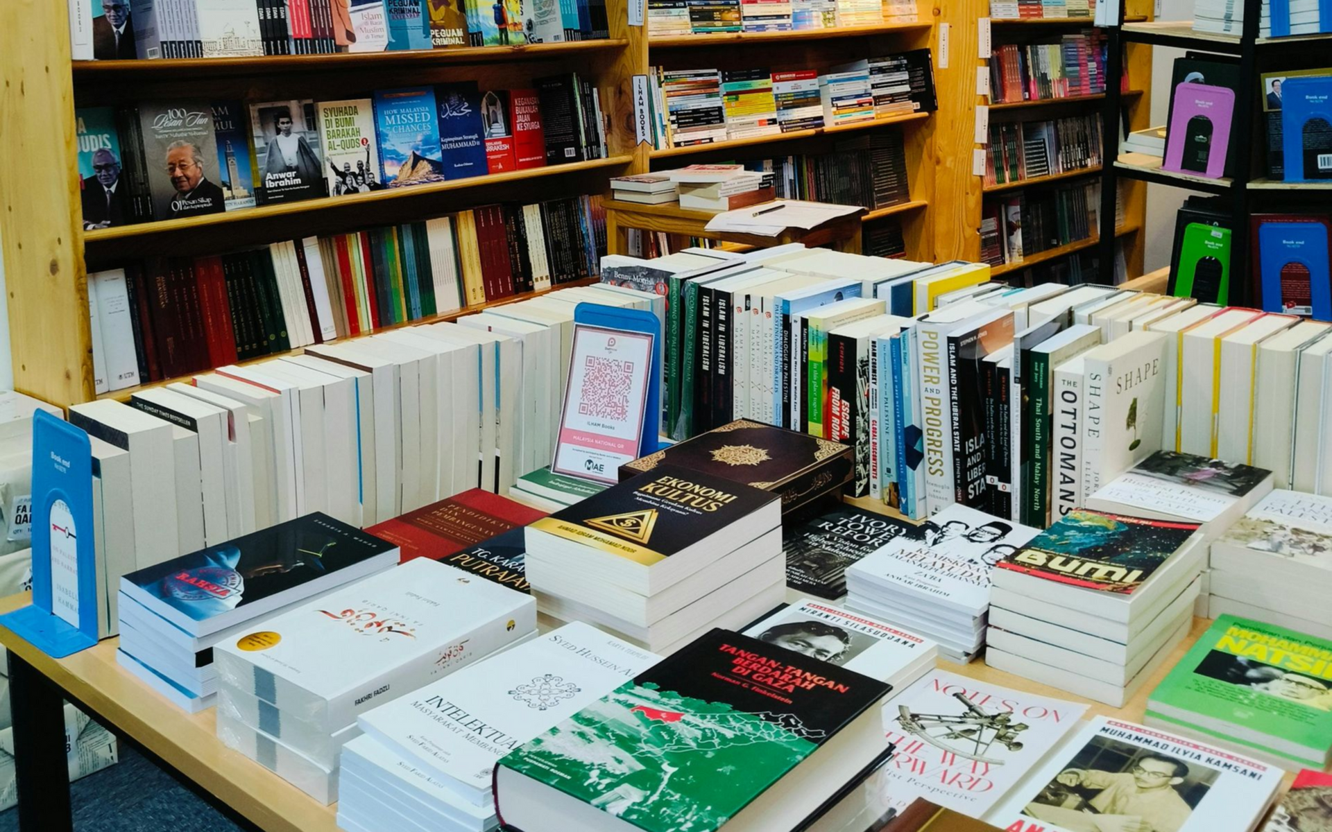 Een boekenwinkelpresentatie met stapels boeken op een tafel en planken vol boeken op de achtergrond.